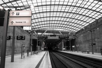 Das Bild zeigt einen Bahnsteig auf Deutsch. Die Station befindet sich wahrscheinlich in Bonn, Deutschland. Das Bild ist in Schwarzweiß gehalten und hat eine monochrome Ästhetik.