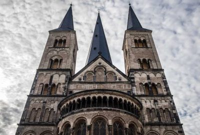 Das Bild zeigt ein großes Steingebäude mit Türmen, genauer gesagt das Bonner Münster. Es weist Elemente der mittelalterlichen und gotischen Architektur auf, darunter Türme und Türmchen. Das Gebäude ist ein Wahrzeichen, das als Kultstätte dient.