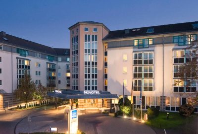 Hotel in Mainz. Das Bild zeigt ein Hotel. Es befindet sich in Mainz und scheint ein Hotel oder ein Geschäftsgebäude zu sein. Das Foto wurde in der Nacht aufgenommen, und in der Umgebung befinden sich Bäume und eine Straße.