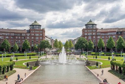 Das Bild zeigt einen Brunnen in einem Innenhof mit Gebäuden im Hintergrund. Die Szenerie ist draußen bei bewölktem Himmel. Der Standort ist Mannheim in Deutschland.