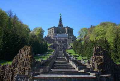 Treppe zum Hügel mit dem Herkules-Denkmal in Kassel, Deutschland, vor dem Hintergrund von Grün und Himmel.