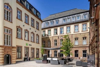 Das Bild zeigt ein Hotelgebäude in Trier, Deutschland. Es verfügt über einen Innenhof und eine architektonische Fassade mit Fenstern.