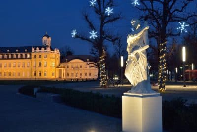 Das Bild zeigt eine Statue in einem Park in Karlsruhe. Es zeigt eine Skulptur vor einem Hintergrund aus Bäumen und dem Nachthimmel im Winter.
