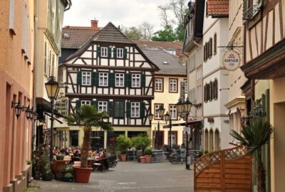 Das Bild zeigt eine Straße in Bad Kreuznach, Deutschland, die durch Gebäude und Bäume geprägt ist. Es hebt Außenelemente wie Fenster und Blumentöpfe hervor.