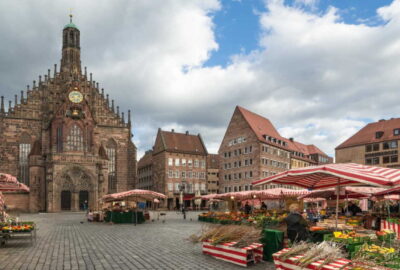 Das Bild zeigt einen geschäftigen Markt auf einem Stadtplatz, auf dem die Frauenkirche in Nürnberg deutlich zu sehen ist.