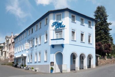 Das Bild zeigt ein blaues Gebäude namens Hotel Höhn in Rüdesheim, Deutschland. Es befindet sich in einer Außenumgebung mit klarem Himmel und sichtbaren Wolken.