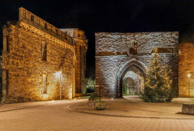 Das Bild zeigt ein Steingebäude mit einem markanten Steinbogen und einem Turm, ein Schloss in Koblenz, Deutschland, mit Ziegelelementen und umgebenden Pflanzen.