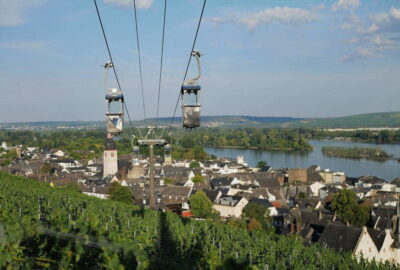 Das Bild zeigt eine Seilbahn über Rüdesheim in Deutschland. Umgeben von natürlicher Schönheit fängt es die Landschaft ein, darunter Bäume, Gras und Wasserelemente wie einen See oder Fluss.