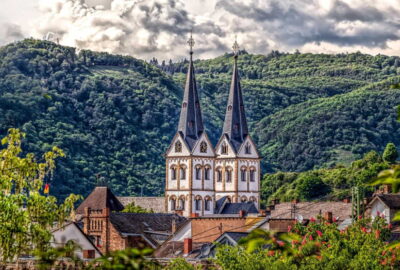 Das Bild zeigt ein großes Gebäude mit markanten Kirchtürmen vor einer Baumkulisse und präsentiert die Landschaft um Boppard in Deutschland.