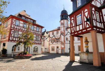 Das Bild zeigt einen Innenhof am Fischmarkt in Alzey, Deutschland, mit Gebäuden rund um einen Brunnen. Die Szene vermittelt mit ihren einzigartigen Fassaden eine charmante Stadtatmosphäre.