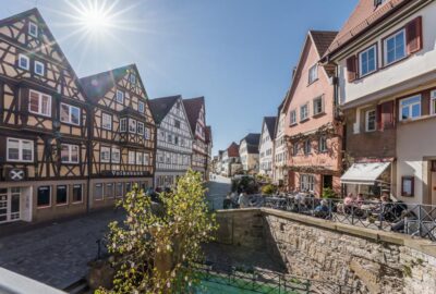 Das Bild zeigt eine Straßenszene in der Heilbronner Altstadt. Gebäude stehen an einer Steinmauer. Die Umgebung scheint ein Wohngebiet innerhalb einer Stadt zu sein und weist regionaltypische architektonische Elemente auf.