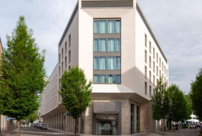 Das Bild zeigt das Hotel Holiday Inn Express in Heilbronn. Vor dem Gebäude stehen mehrere Bäume, die für eine angenehme Atmosphäre sorgen.