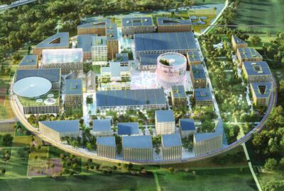 Das Bild zeigt eine Luftaufnahme des Innovationsparks AI in Heilbronn. Es zeigt eine Mischung aus urbanem Design mit üppigem Grün und verschiedenen Gebäuden. Die Perspektive hebt sowohl Wohnhäuser als auch Gewerbegebäude innerhalb des Stadtbildes hervor.