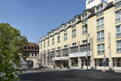 Das Maritim Hotel Würzburg ist ein Gebäude in Deutschland, dessen Fassade mit der umgebenden Straße und den Bäumen interagiert.