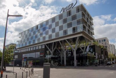 Das Bild zeigt ein großes Geschäftsgebäude in Metz, Frankreich, das durch seine Glasfenster charakterisiert ist. Umgeben von einem Ballungsgebiet.