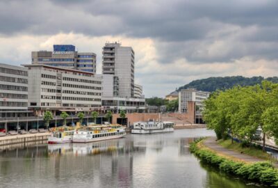 Das Bild zeigt eine Flussszene in Saarbrücken, auf der Boote durch das Wasser navigieren. Um den Fluss herum sind Bäume und Gebäude zu sehen, die zu einer malerischen Stadtlandschaft beitragen.