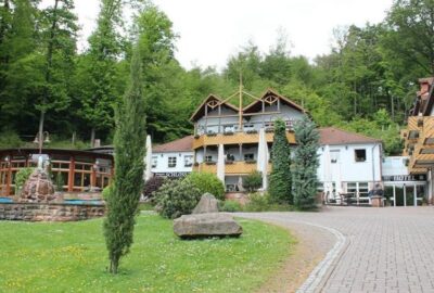 Das Bild zeigt das Schlosshotel Landstuhl in Deutschland, ein Gebäude, das von üppigem Grün und Bäumen umgeben ist.