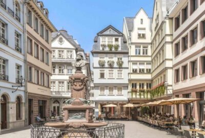 Das Bild zeigt einen Innenhof in der Frankfurter Altstadt mit umliegenden Gebäuden. Es verfügt über eine Mischung aus architektonischen Stilen und Elementen wie Fenstern, Statuen und einem Stadtplatz. Die Szene fängt eine Mischung aus historischen und modernen Strukturen im Stadtzentrum ein.