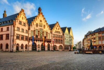 Das Foto zeigt einen Römer mit vielen Fenstern im Vordergrund. Die Einstellung scheint im Freien mit bewölktem Himmel zu sein. Zu den mit dem Bild verknüpften Tags gehören Gebäude, Fenster, Straße und Stadt.